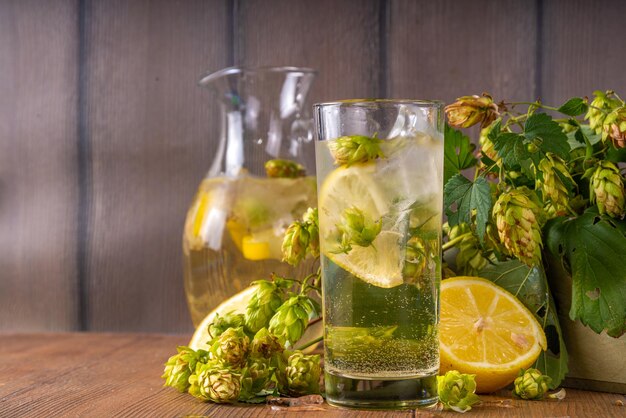 Ziołowa lemoniada z szyszek chmielowych i kwiatów Organiczny surowy alternatywny zimny napój ze świeżymi szyszkami chmielowymi cytryną i lodem na drewnianym stole