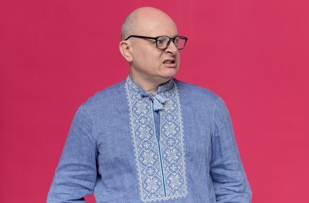Zirytowany dorosły słowiański mężczyzna w niebieskiej koszuli w okularach optycznych, patrząc z boku