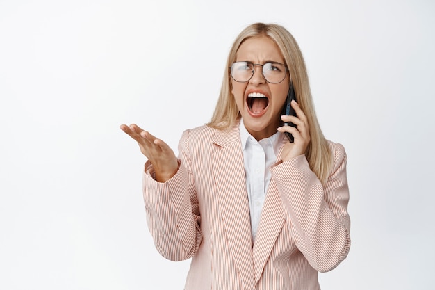 Zła krzycząca pani z biura, kłócąca się przez telefon, krzycząca i kłócąca się z rozmówcą, stojąca w garniturze na białym