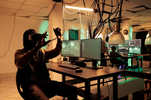 Złodziej programujący wirusa komputerowego w zestawie słuchawkowym vr, łamiący hasło do bazy danych w Metaverse za pomocą interaktywnych okularów 3D. Haker kodujący złośliwe oprogramowanie w gadżecie wirtualnej rzeczywistości w nocy.