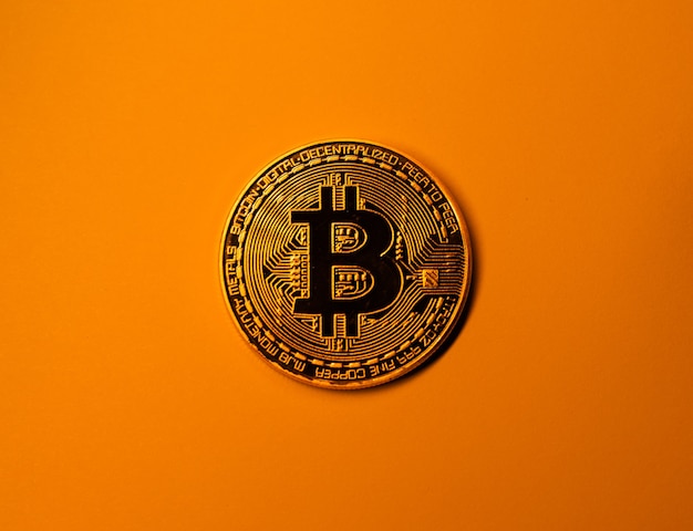 Złota moneta bitcoin na żółtym monochromatycznym kolorze.