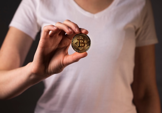 Złota moneta BTC lub bitcoin trzymana w kobiecej dłoni.