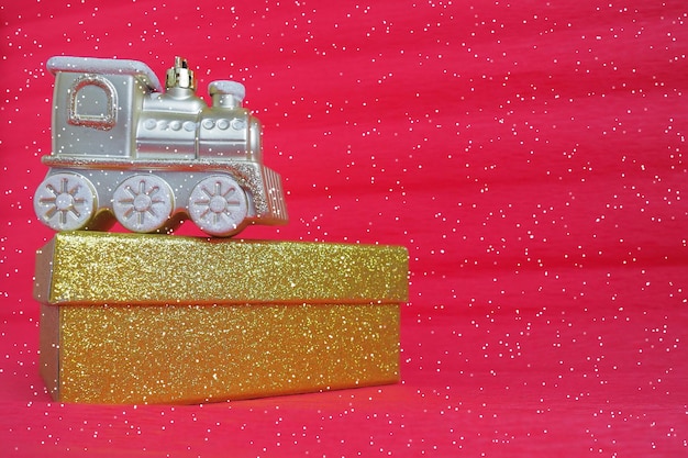 Złota zabawka pociągu lokomotywa i pudełko na czerwonym tle gradientu Nowy rok lub kartka świąteczna Sople i śnieg w pociągu Wolne miejsce na tekst Skopiuj miejsce Spadające płatki śniegu