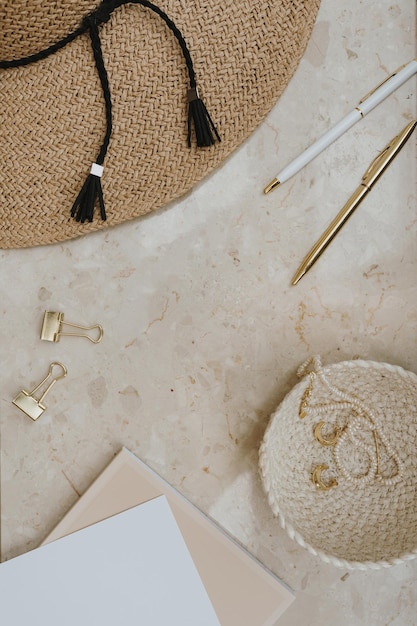 Złote akcesoria ze słomianego kapelusza na marmurowym stole z pustą makietą miejsca na kopię Stylowa moda płaski widok z góry minimalistyczny szablon obszaru roboczego biurka domowego