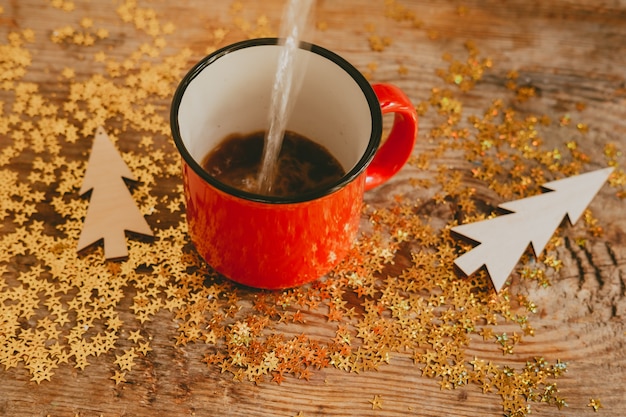 Złote iskierki i drewniane choinki na drewnianym tle. Boże Narodzenie tło wykonane z błyszczy i czerwonych filiżanek z kawą. Woda wlewa się do kubka.