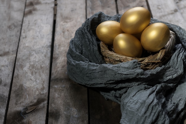 Złote jajka w gnieździe na ciemnym rocznika drewnianym stole