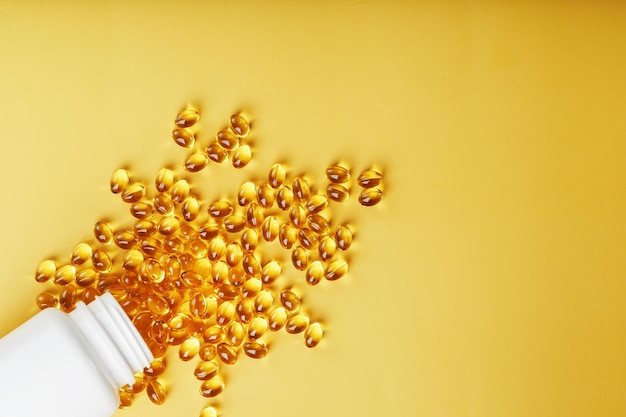 Złote kapsułki witaminy D3 wylane ze słoika na żółtym tle z wolną przestrzenią