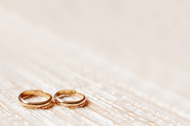 Złote obrączki na beżu. Szczegóły ślubne, symbol miłości i małżeństwa.