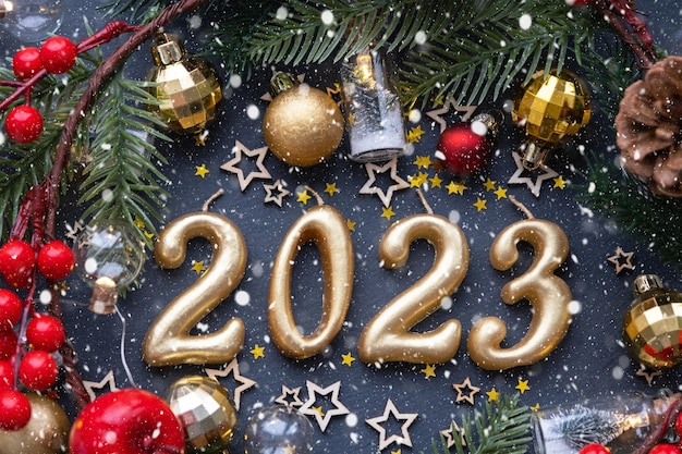 Złote postacie 2023 wykonane ze świec na czarnym kamiennym tle łupków ozdobione są świątecznym wystrojem gwiazd cekinów gałęzie jodły kulki i girlandy Kartkę z życzeniami szczęśliwego nowego roku
