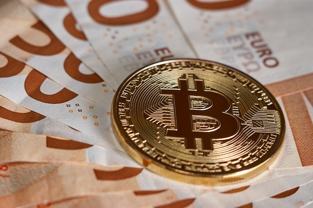 Złoty bitcoin na tle banknotów pięćdziesiąt euro. Kryptowaluta Bitcoin, technologia Blockchain, pieniądze cyfrowe