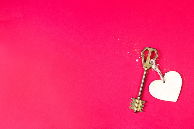 Złoty klucz z drewnianą przywieszką w kształcie serca na czerwonym tle