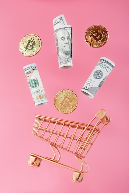 Złoty mini wózek z bitcoinami i dolarami amerykańskimi w locie lewitacji na różowej powierzchni
