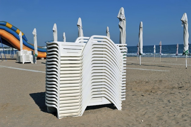 Złożone leżaki i zamknięte parasole na bezludnej morskiej piaszczystej plaży w godzinach porannych.