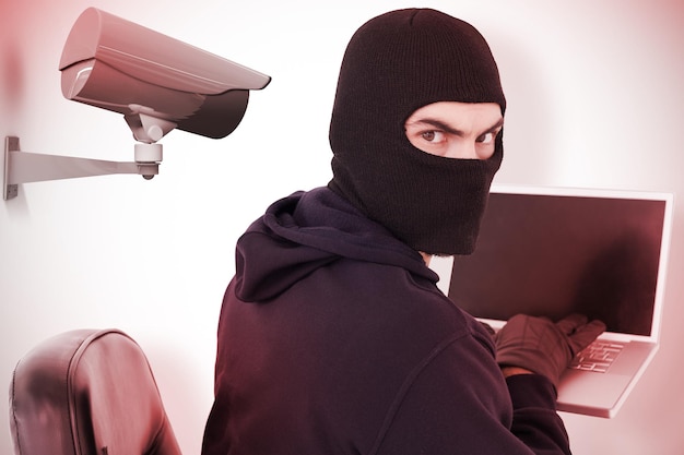 Złożony obraz hakera siedzącego i włamującego się do laptopa