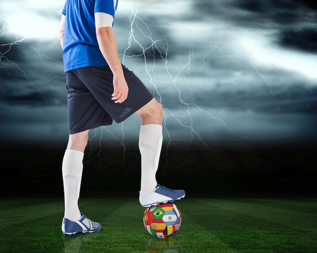Złożony wizerunek gracza futbolu stojącego z międzynarodową piłką przeciwko boisku piłkarskim pod burzliwym niebem