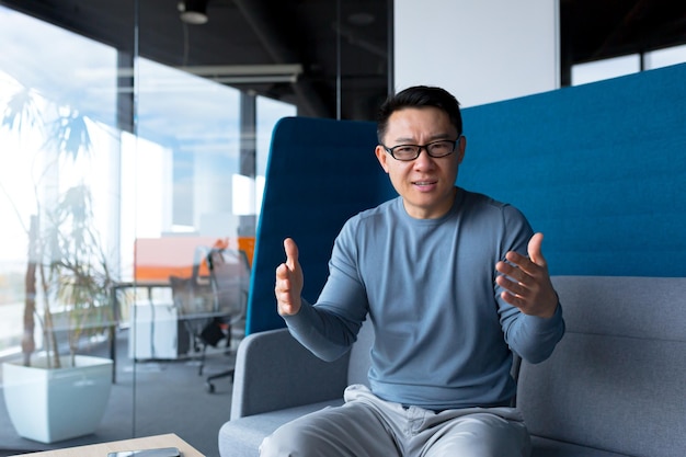 Zły i poważny azjatycki mężczyzna rozmawiający podczas rozmowy wideo freelancer patrzący na kamerę internetową biznesmen pracujący w nowoczesnym biurze