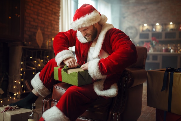 Zły pijany Mikołaj otwiera prezenty pod choinką
