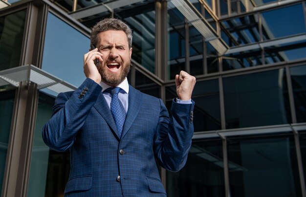 Zdjęcie zły przedsiębiorca w garniturze krzyczy podczas rozmowy telefonicznej poza biurem frustracja