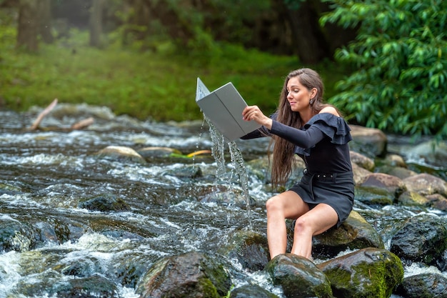 Zmartwiona kobieta wyciąga z wody laptopa, który wpadł do rzeki, wypadek na wakacjach na odległość