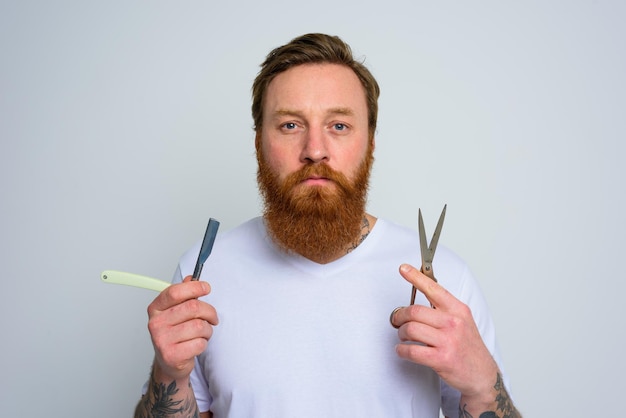 Zdjęcie zmartwiony mężczyzna z nożyczkami i ostrzem jest gotowy do obcięcia brody