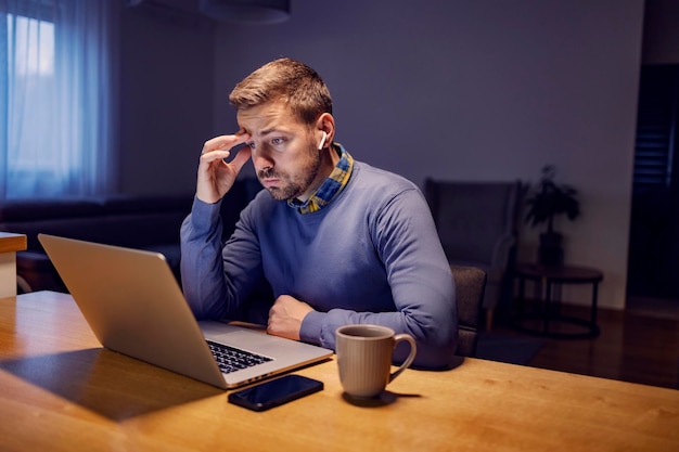 Zmartwiony przedsiębiorca patrzący na laptopa w domu i próbujący znaleźć rozwiązanie