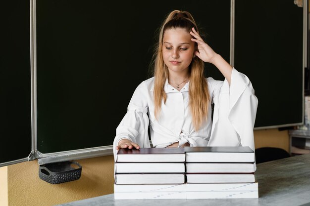 Zmęczona i sfrustrowana uczennica leży na książkach przy tablicy w szkole Edukacja szkolna Dziewczyna jest zmęczona odrabianiem prac domowych