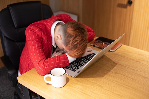 Zmęczona kobieta pracująca w biurze śpi na klawiaturze laptopa.