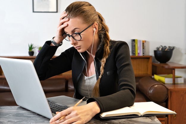 Zmęczona kobieta z okularów słuchawki i laptopa studiuje pracę