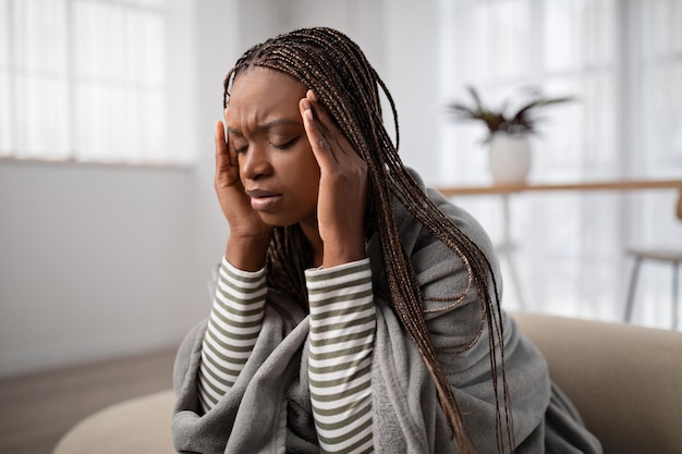 Zmęczona młoda czarna kobieta cierpiąca na ból głowy w domu