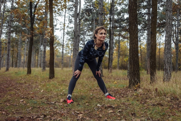 Zdjęcie zmęczona sportowa sprawna kobieta z warkoczykami odpoczywa po joggingu w lesie jesienią