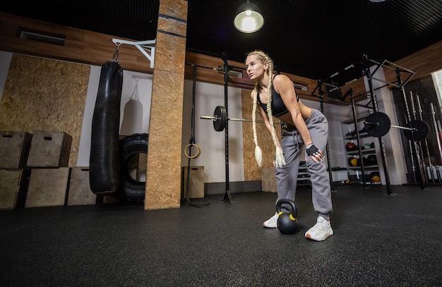 Zmęczona sprawna kobieta odpoczywa po intensywnym treningu z kettlebell w nowoczesnej siłowni Trening funkcjonalny