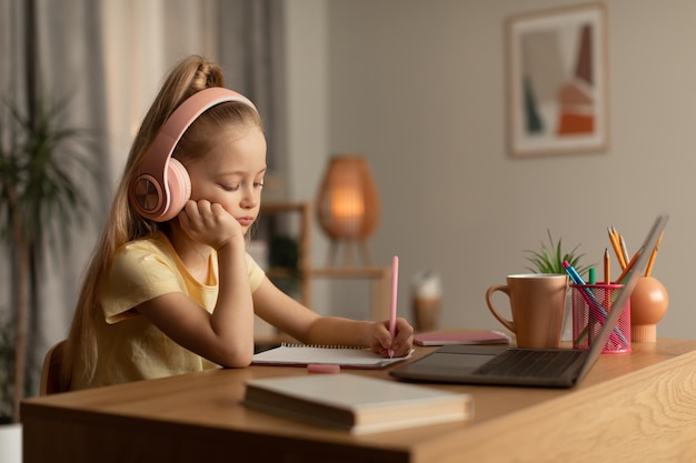 Zmęczona uczennica uczy się online za pomocą laptopa i robi notatki w pomieszczeniu