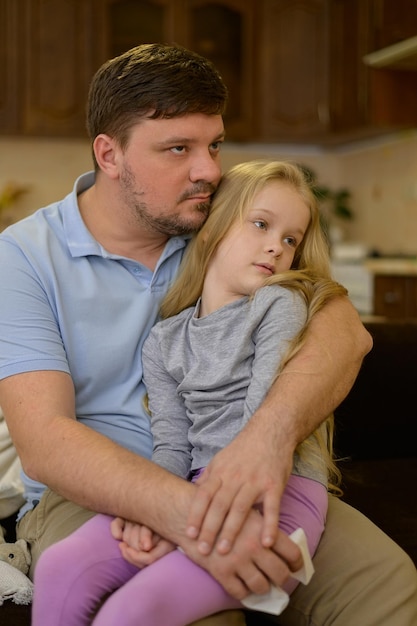 Zmęczone chore dziecko siedzi na kolanach ojca na kanapie w domu ojciec podejrzewa, że jego córka