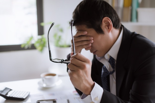 Zmęczony Azjatycki Młody Biznesmen Uczucie Stresu I Zdejmowania Okularów Odczuwa Zmęczenie Oczu Po Długiej Pracy Biurowej Na Komputerze, Przepracowaniu, Syndromie Biura, Problemach Biznesowych I Koncepcji Finansowej