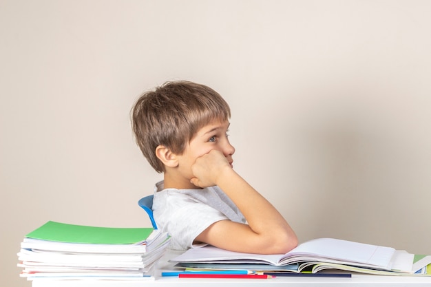 Zmęczony chłopiec siedzi przy stole z podręczników szkolnych i myślenia