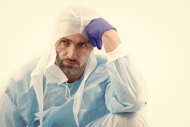 Zmęczony człowiek lekarz epidemiolog w ochronnym kostiumie ochronnym podczas pandemicznej kwarantanny koronawirusa na białym tle, myśląc o lekarstwie tworzącym szczepionkę