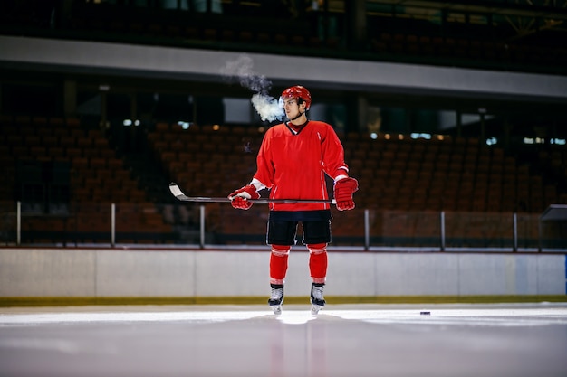 Zdjęcie zmęczony hokeista stojący na lodzie z kijem w rękach w hali.