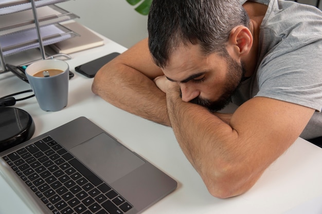 Zdjęcie zmęczony mężczyzna opierając głowę o biurko w domu