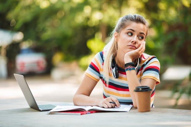 Zmęczony student młoda dziewczyna siedzi w parku przy użyciu komputera przenośnego pisania notatek.