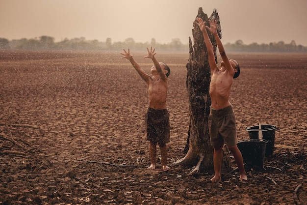 Zmiany klimatyczne Azjatyccy chłopcy cieszą się pierwszym opadającym sezonem deszczowym na suchej, popękanej ziemi Ochrona środowiska i powstrzymanie koncepcji globalnego ocieplenia