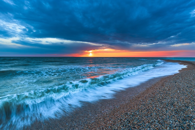 Zdjęcie zmierzch na plaży z długą linią brzegową, słońcem i dramatycznym niebem