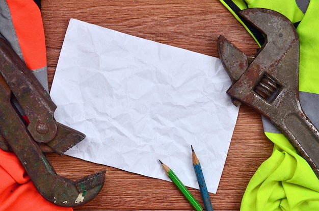 Zmięty arkusz papieru z dwoma ołówkami otoczony zielonymi i pomarańczowymi mundurami roboczymi i kluczami nastawnymi
