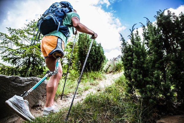 Zmotywowany aktywny turysta męski z protezą podnoszący się podczas próby nordic walking