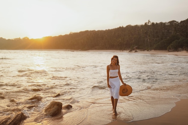 Zmysłowa dziewczyna spacerująca po plaży przed idealnym zachodem słońca podczas wakacji