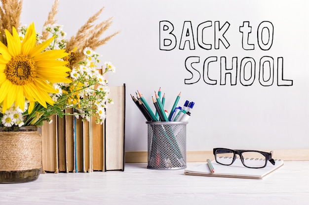 Zdjęcie znacznik napisów na białej tablicy, back to school stolik z książkami, bukietem kwiatów, szklankami i atrybutami do pisania.