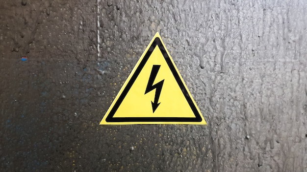 Znak bezpieczeństwa żółty i czarny na srebrnym tle metalu. Błyskawica wysokiego napięcia w trójkącie przestroga niebezpieczeństwo śmierć prądu.