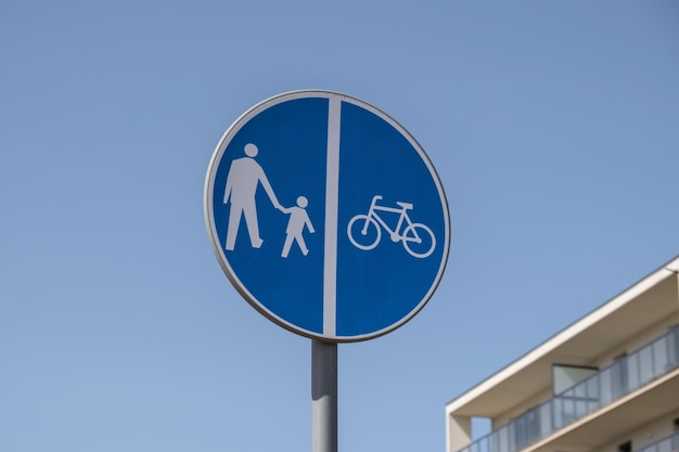 Znak podziału trasy dla rowerzystów i pieszych Znak drogowy Pieszy i rowerzyści mogą przejść przez ulicę tutaj na tle błękitnego nieba