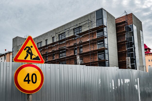 Znak "prace naprawcze" i "ograniczenie prędkości" na tle budowy wielokondygnacyjnego budynku z rusztowaniem.