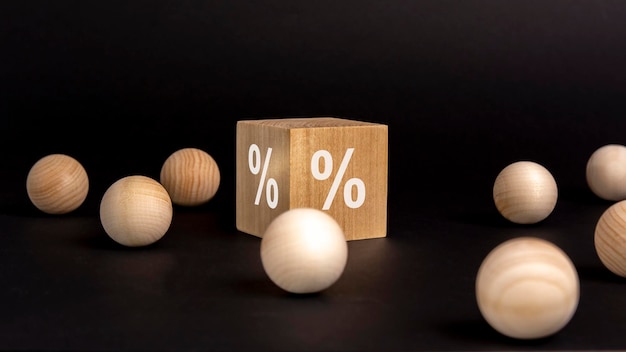 Znak procentu na drewnianym sześcianie na czarnym tle z drewnianymi kulkami koncepcja sprzedaży i rabatu