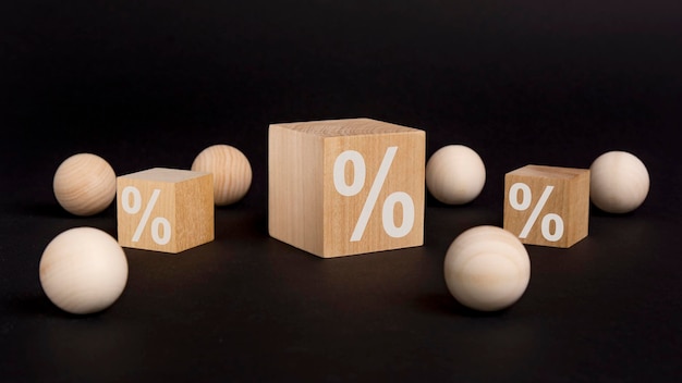 Znak procentu na drewnianym sześcianie na czarnym tle z drewnianymi kulkami koncepcja sprzedaży i rabatu